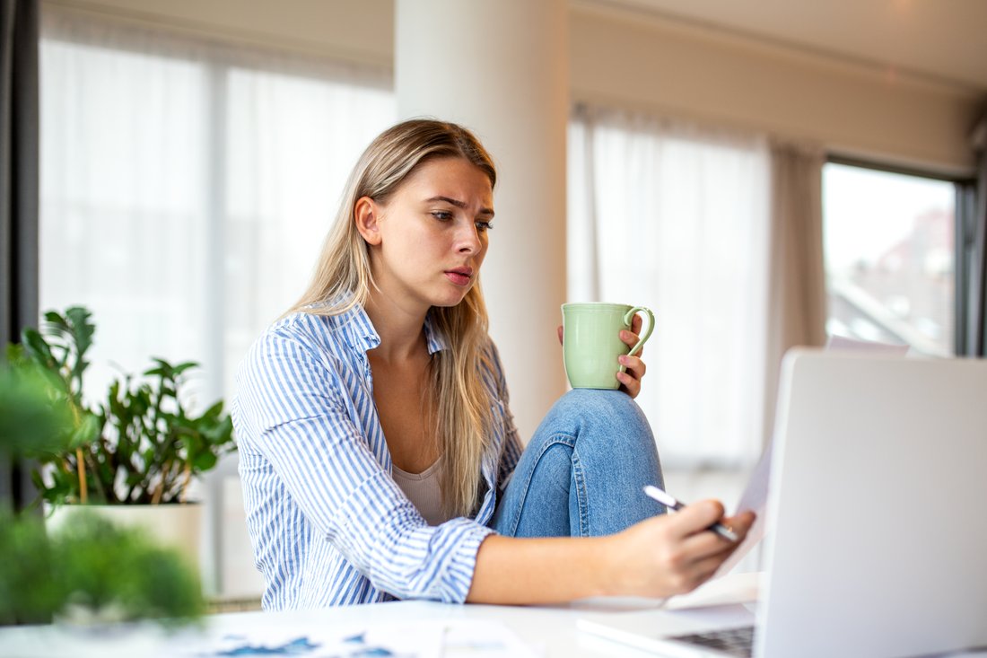 Młoda kobieta czyta coś na laptopie, w ręku kubek