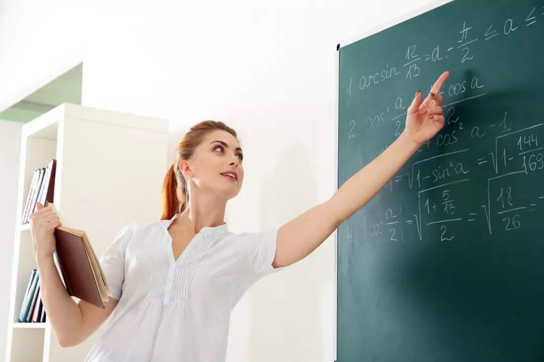 Young teacher standing beside a blackboard in a school classroom.