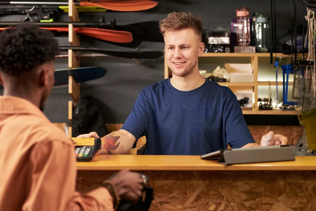 Mlody sprzedawca obsluguje klienta przy kasie w sklepie