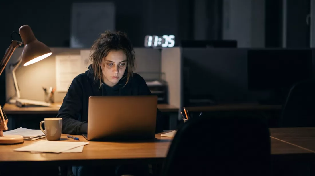 Mloda kobieta pracuje wieczorem przy laptopie w pustym, przyciemnionym biurze