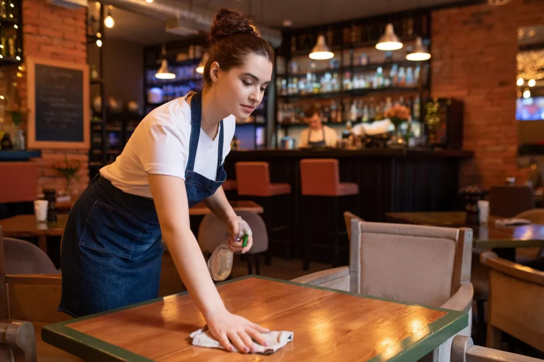 Młoda kelnerka przeciera stolik w restauracji podczas wieczornej zmiany