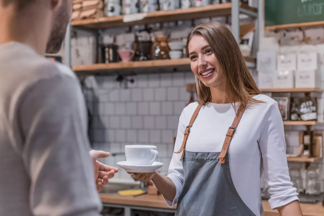 Mloda baristka podaje filizanke kawy klientowi w kawiarni.