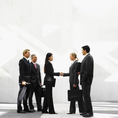 Two Young Businesswomen Shaking Hands With Business Executives Beside Them